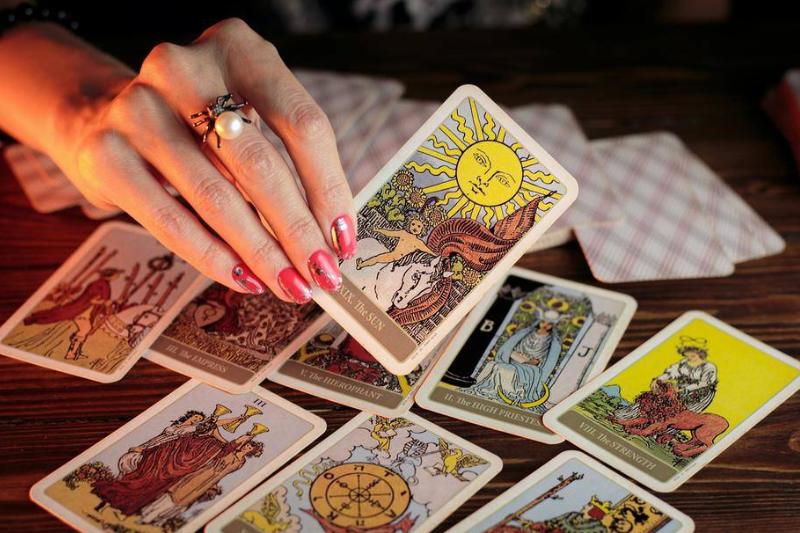 Some tarot cards laid out with a hand holding up The Sun card.