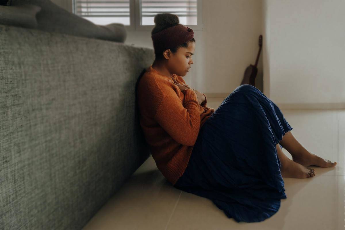 A woman sitting against the back of a couch on the floor, hands over her heart.