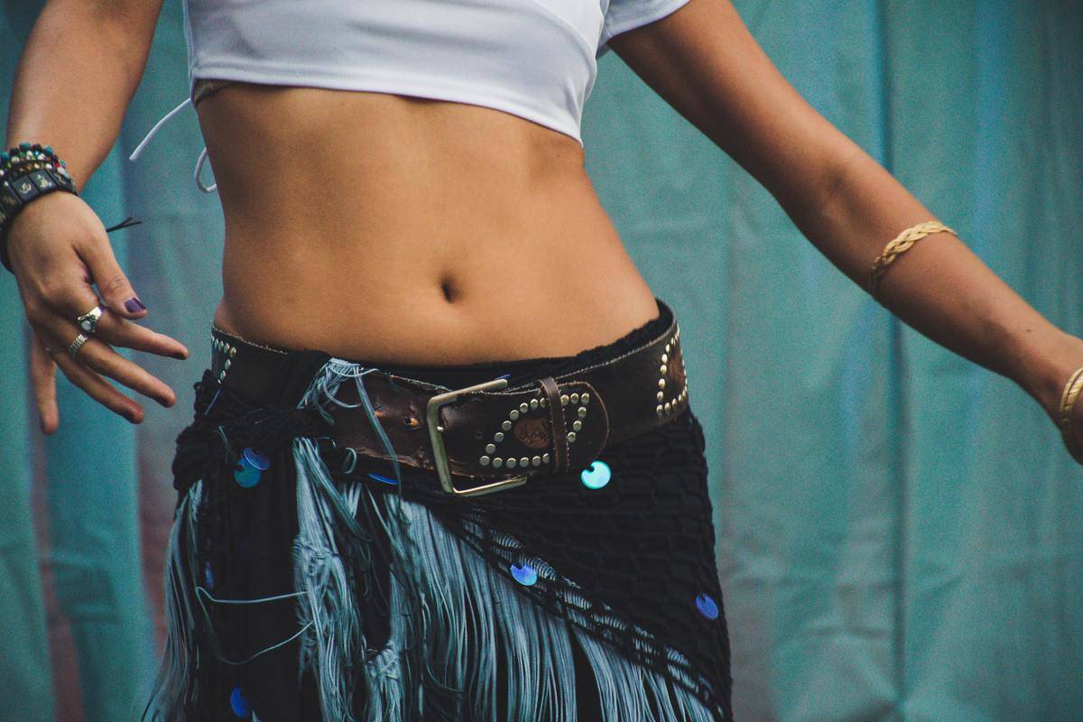 A woman in a cropped white shirt and a blue skirt dancing, close up on her torso.