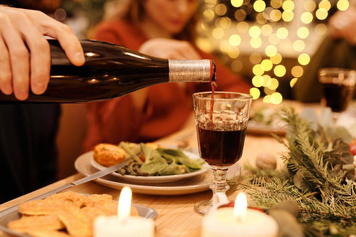 Someone pouring wine into a glass at a Christmas dinner table.