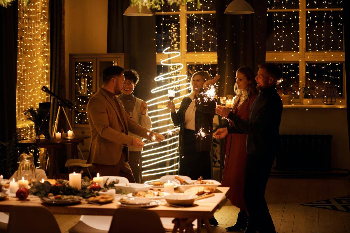 A group of people attending a Christmas party, a table full of food in front of them and a minimalist light-up tree behind them.