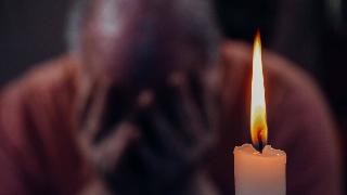 man holds his face in sadness by burning candle
