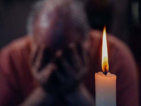 man holds his face in sadness by burning candle