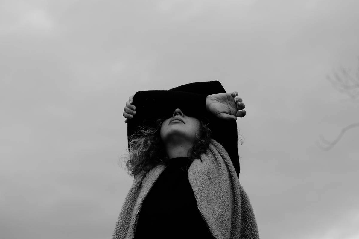 A greyscale image of a woman looking up to the sky, arms folded over her face. 