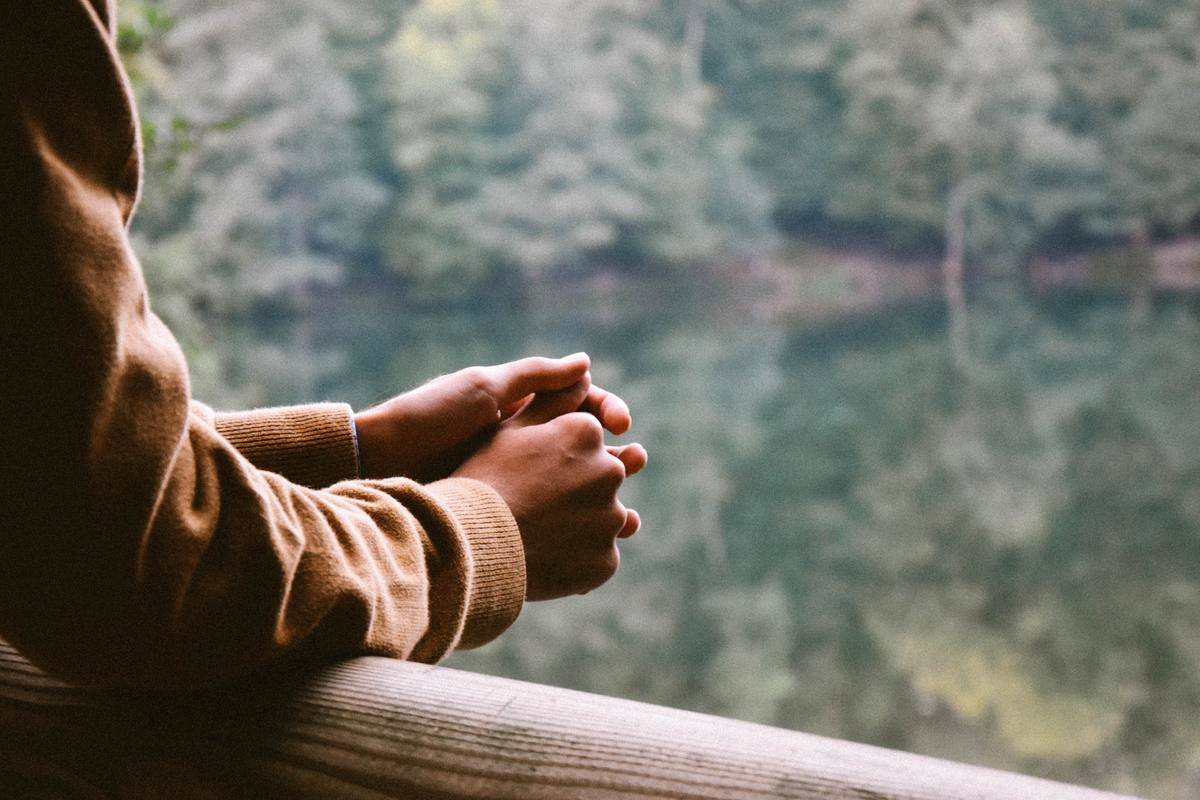 Someone leaning on a wooden railing, looking out towards a lake surrounded by trees. 