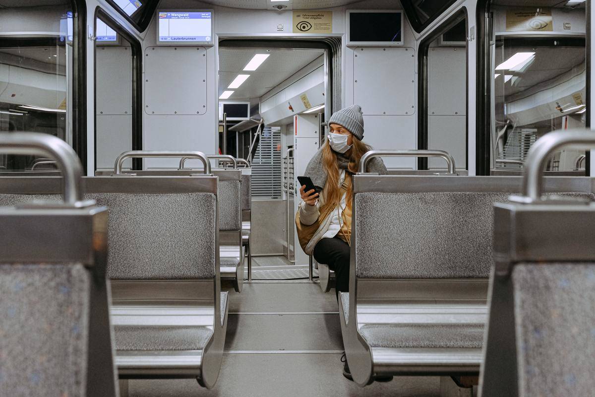 A woman sitting on an empty train car, wearing a mask and looking out the window.