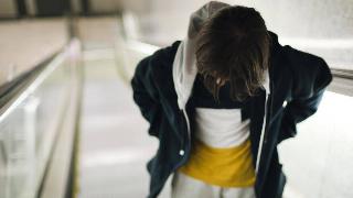 A young person on an escalator, hands in their pockets, looking downward.