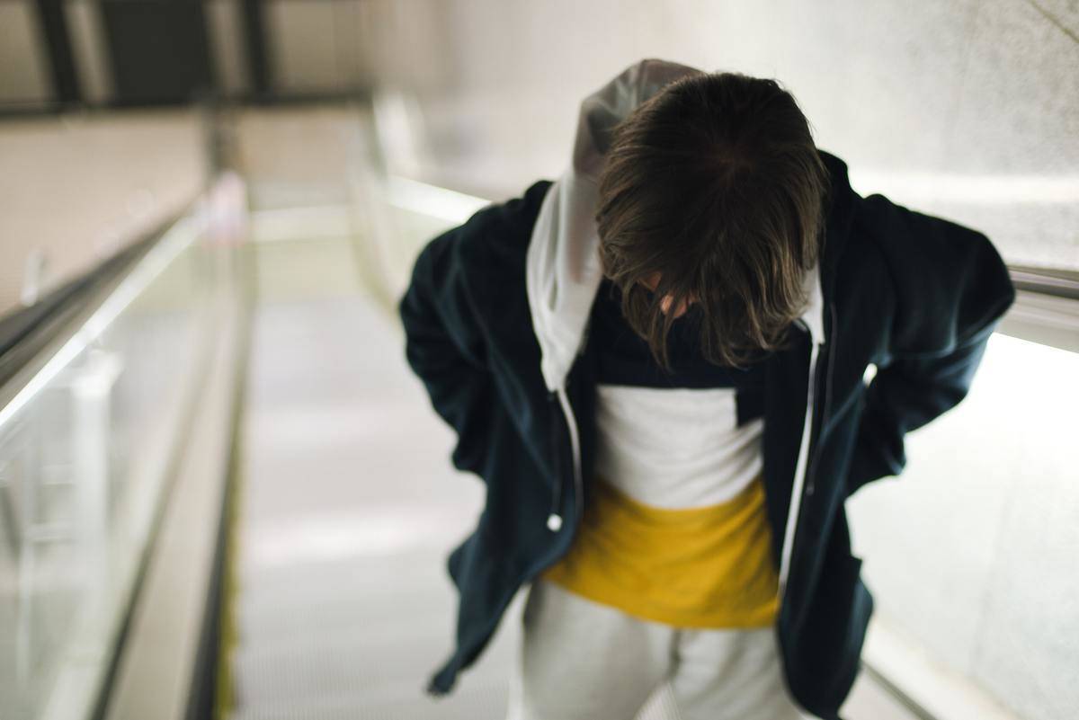 A young person on an escalator, hands in their pockets, looking downward.