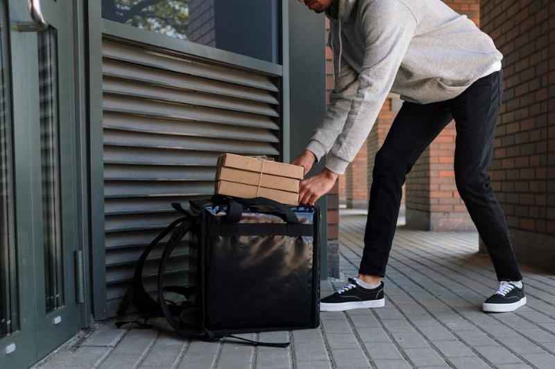 A man dropping off a food delivery in front of someone's door. 