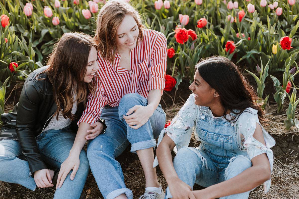 Three women sitting among flowers and laughing.