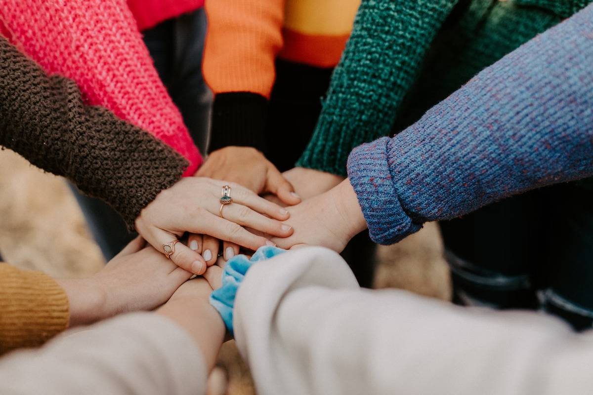 People in a variety of colored sweaters all putting their hands together.