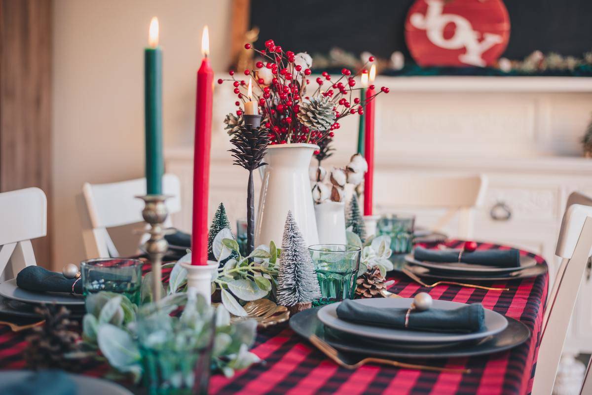 A table set up for Christmas dinner, featuring red and green candles next to tiny trees.