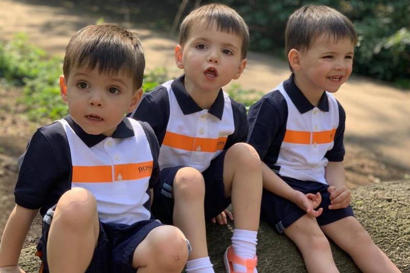 triplets sitting on a rock in matching outfits
