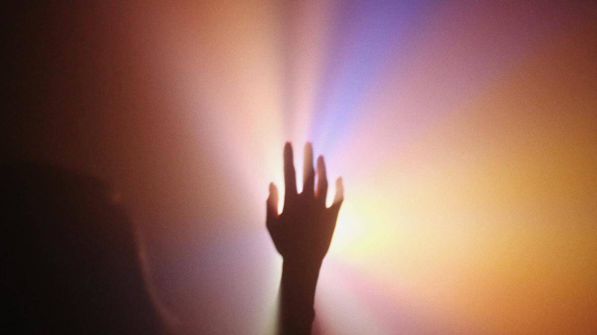 A silhouette of a hand in the middle of a multicolored beam of light.