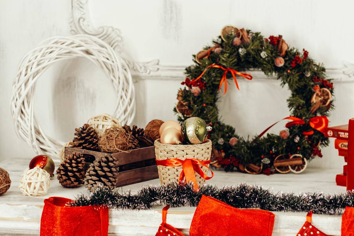 A decorated mantle with two wreathes, some ornaments, some garland, and some pinecones.