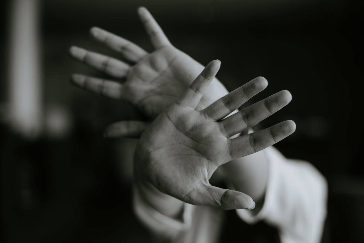 A greyscale image of someone holding their hands up, blocking their face. 