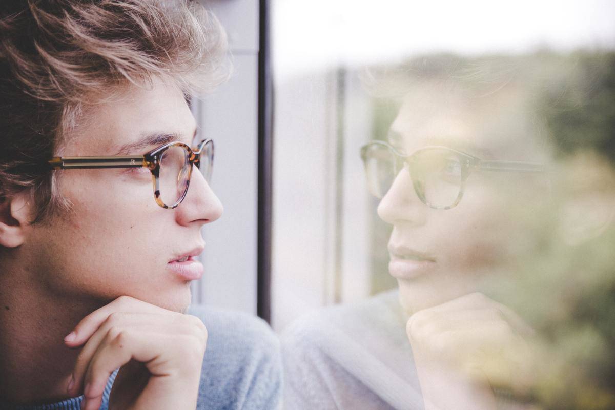 A man looking into a window, his reflection staring back.