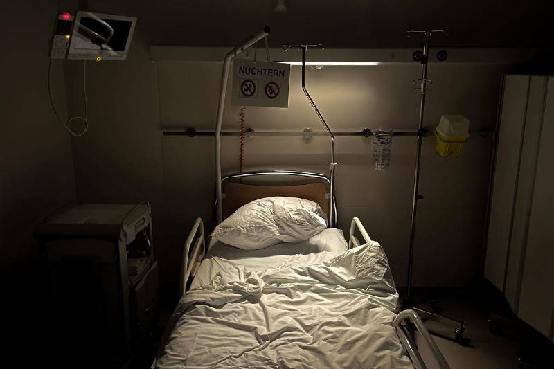 A hospital bed in the dark being lit by one overhead light.