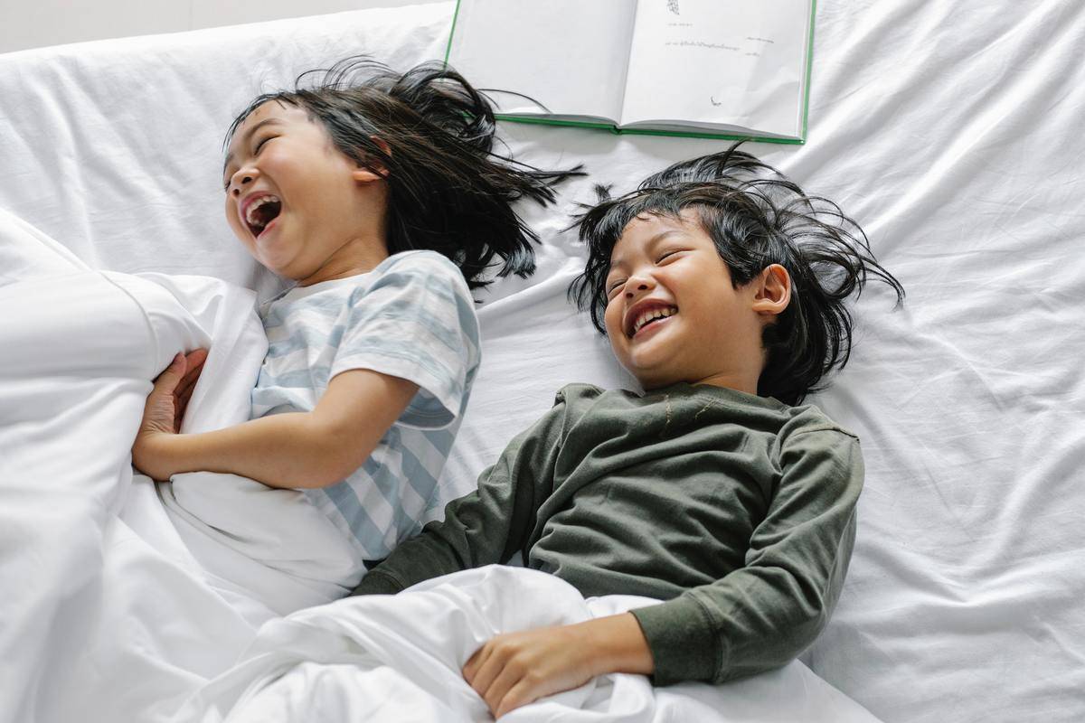 Two kids laying in bed laughing together.