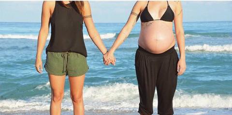 Melanie and Vanessa holding hands on the beach, showcasing Melanies pregnancy.