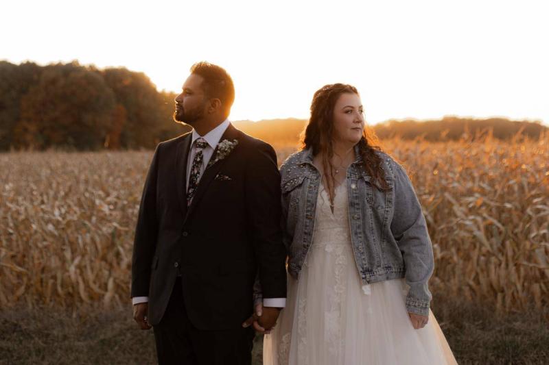 A couple standing together in front of a corn field, holding hands.