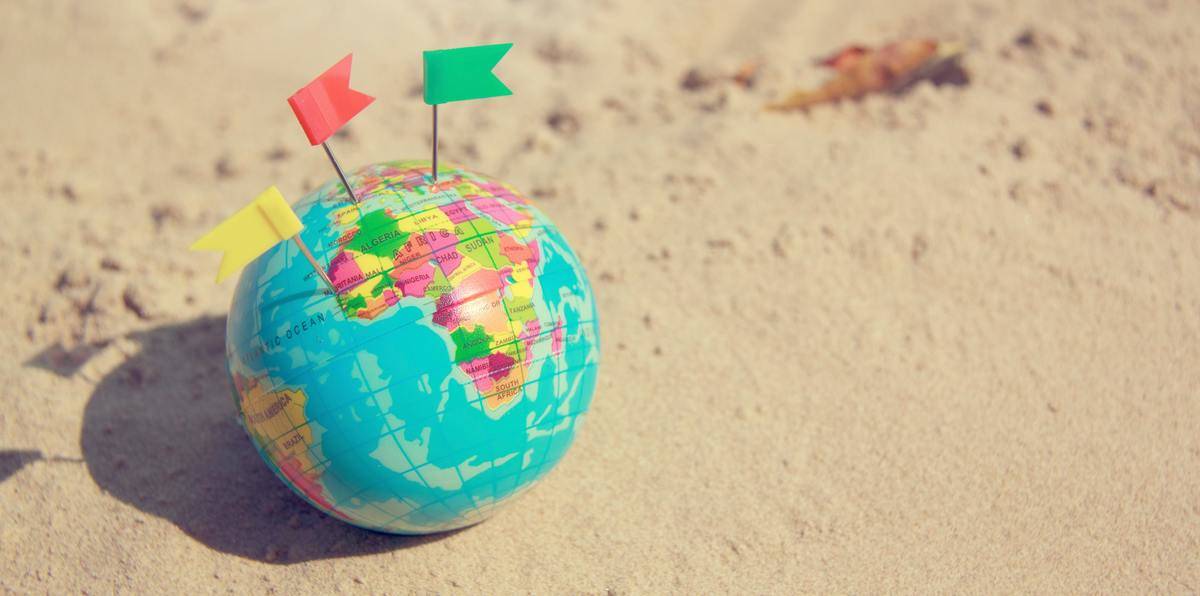 A globe sitting in the sand, three paper flags stuck in it.