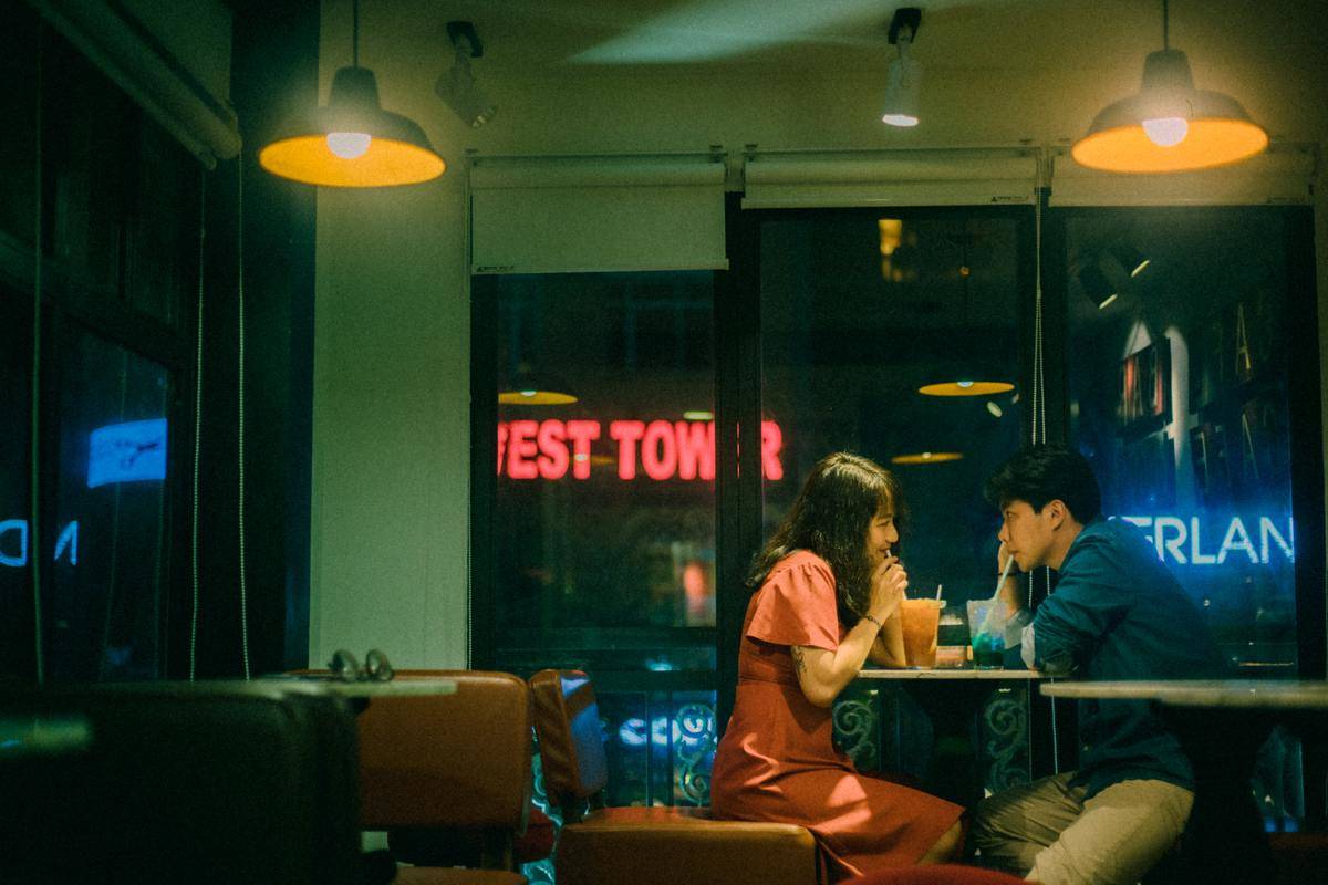 Two young people sat at a restaurant table, each sipping from their own drinks while looking at each other.