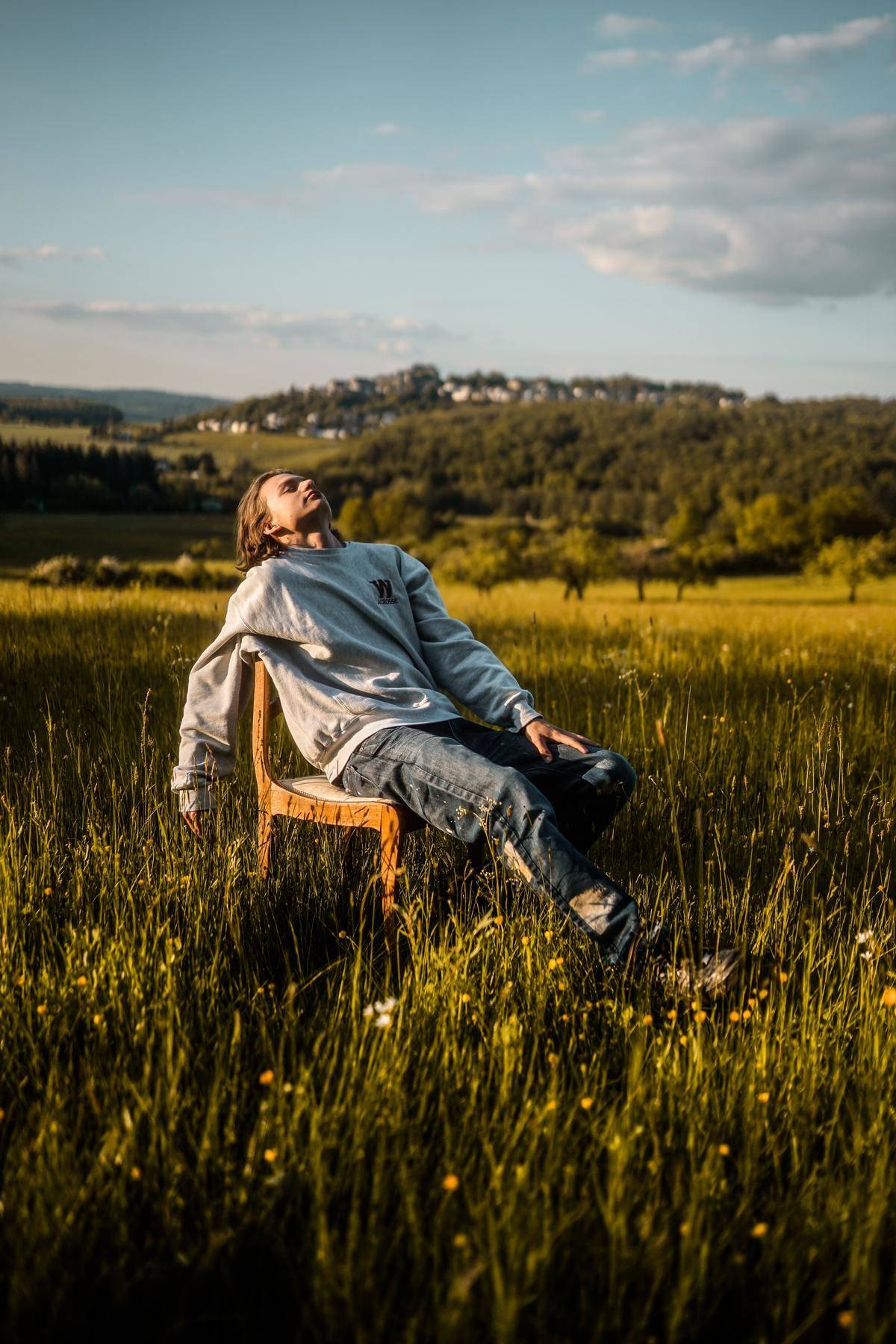 A man sitting in a chair in the middle of a field, the sun shining down on him.
