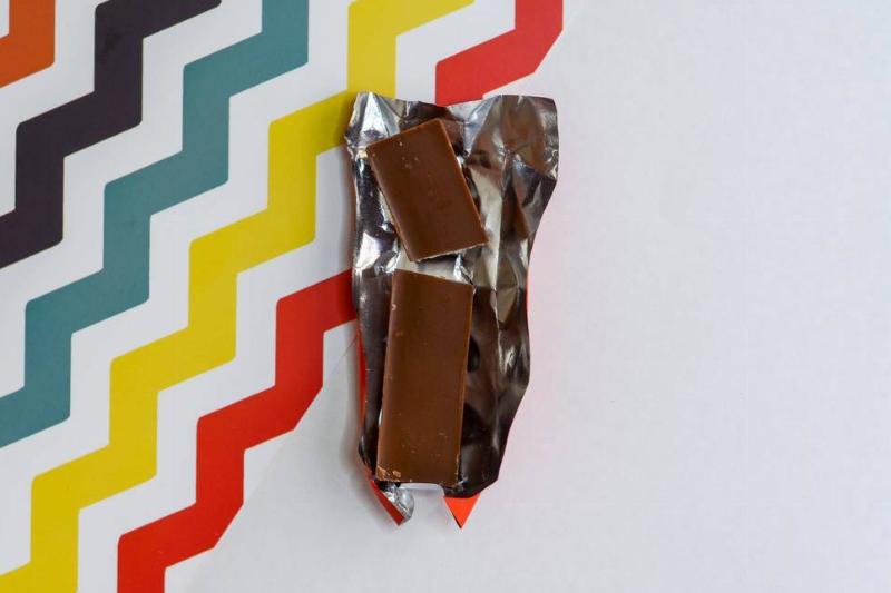A chocolate bar atop it's wrapper with a colorful, striped background behind it.