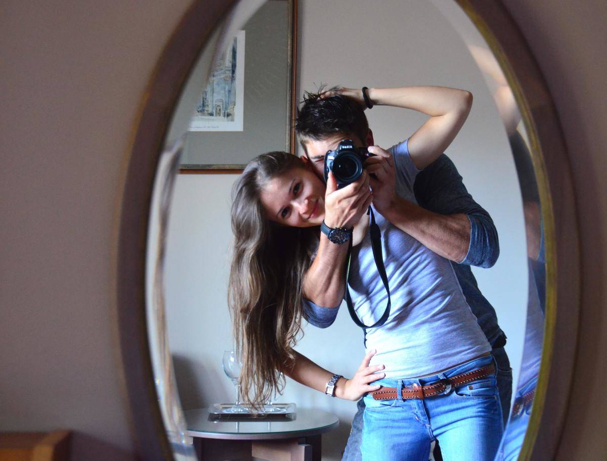 A couple taking a selfie in a mirror, the man holding a professional camera in front of his face.