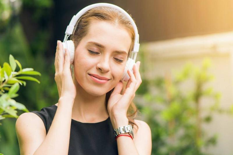 A woman smiling as she listens to music through a pair of headphones.