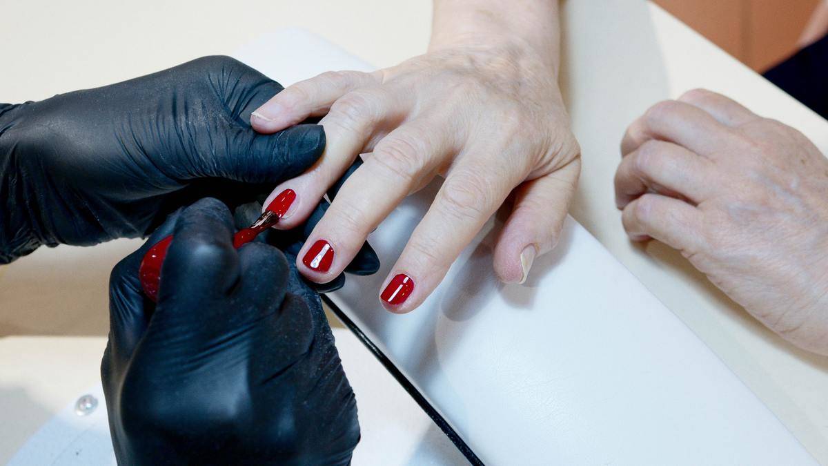A woman getting her nails painted red by a manicurist.