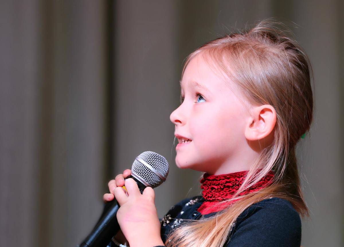 A young girl holding a microphone, looking upwards.
