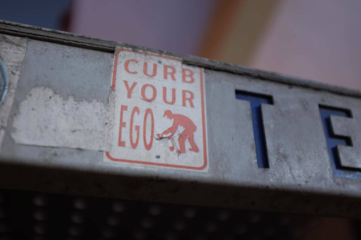 A sticker on a sign that said 'curb your ego'.