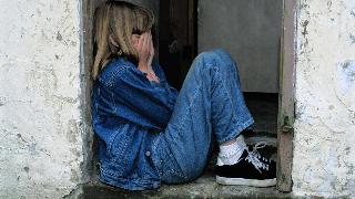 A child sitting in a doorway, hands to her face in distress.