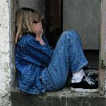 A child sitting in a doorway, hands to her face in distress.
