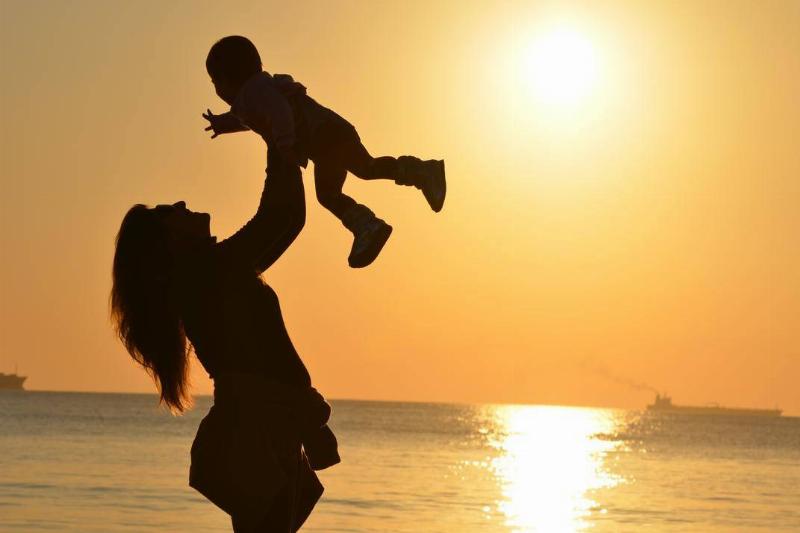 A silhouette of a woman lifting her baby up above her against an orange sunset sky.