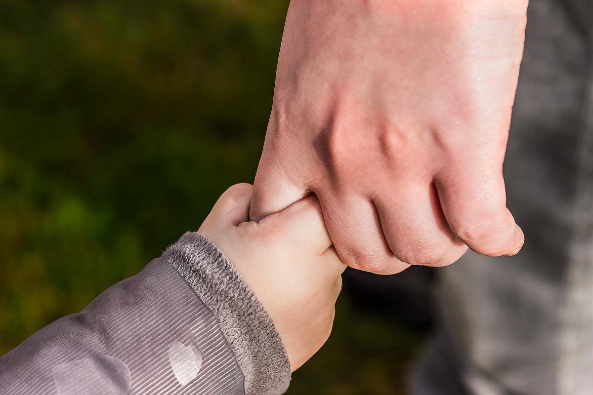 A child's hand holding the finger of an adult hand.