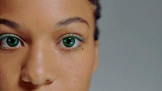 A closeup of a woman's eyes and nose. She's wearing bright green contacts and light green eye makeup.