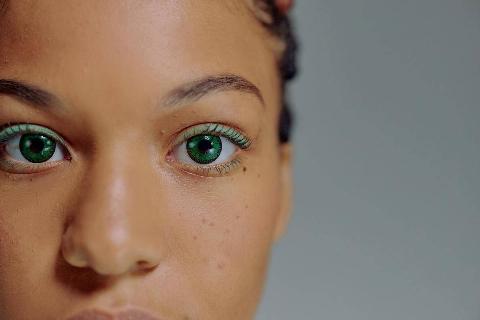 A closeup of a woman's eyes and nose. She's wearing bright green contacts and light green eye makeup.
