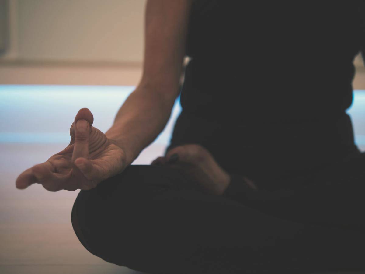 Someone sitting in a meditative pose, focused on their hand resting on their knee.
