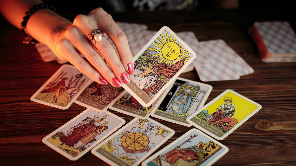 A hand holding The Sun tarot card above an assortment of other cards.