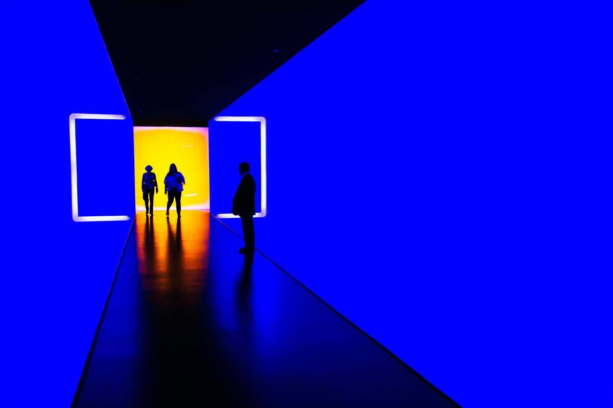 People walking through an art exhibit that features a bright blue tunnel leading to a yellow room.