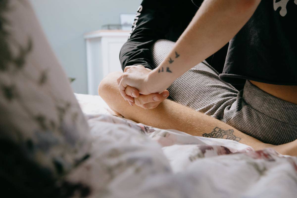 A couple sitting on a bed, legs intertwined and hands holding each other's.