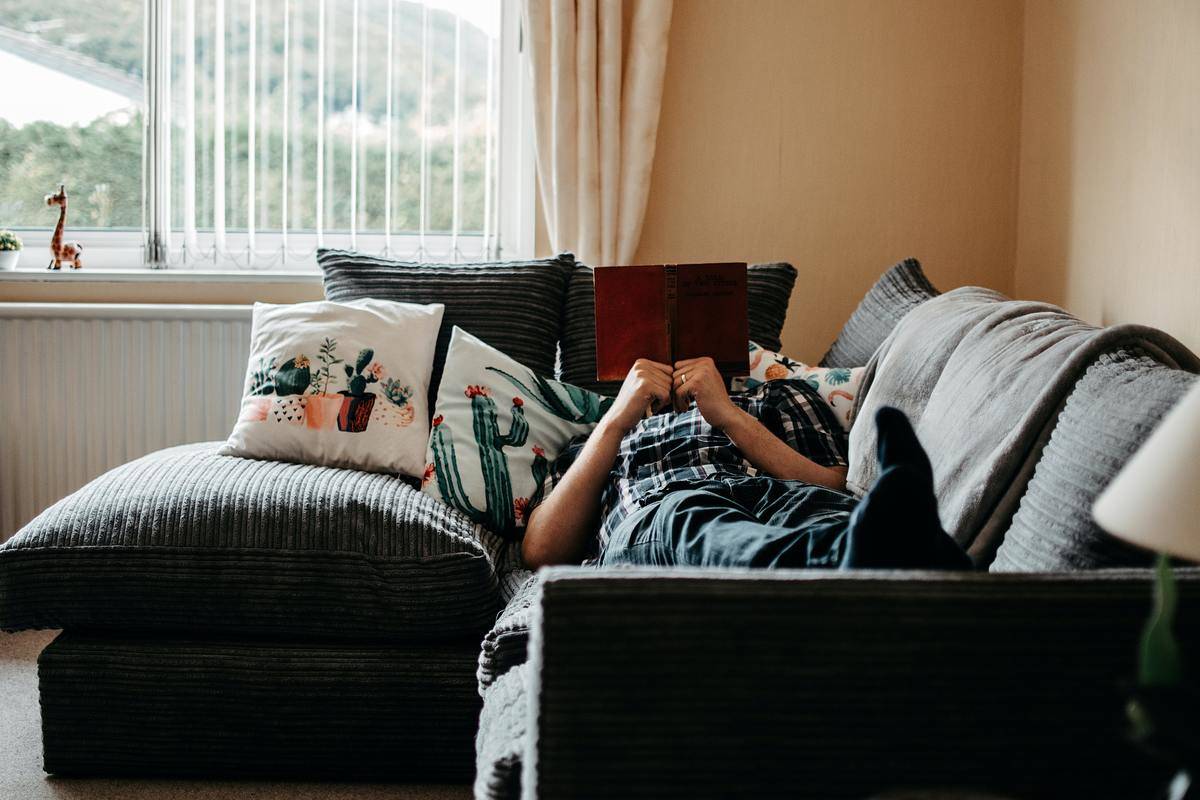 A person lounging on a couch reading a book, holding it over their face.