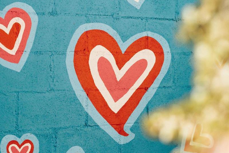 A brick wall painted bright blue with colorful red, white, and pink hearts.