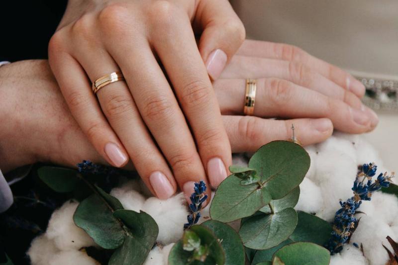 Two hands folded over a bouquet of flowers, both sporting wedding bands.