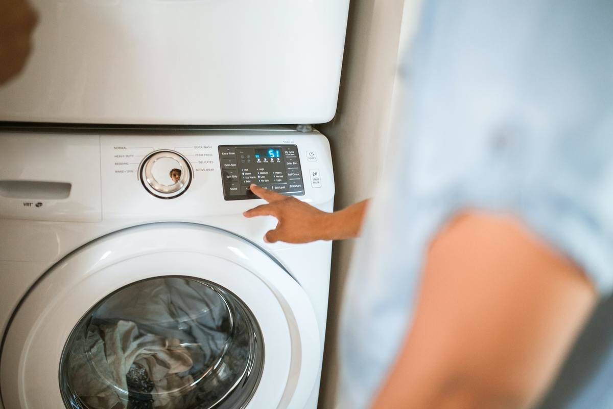 A man reaching out and pushing a button on a washing machine.