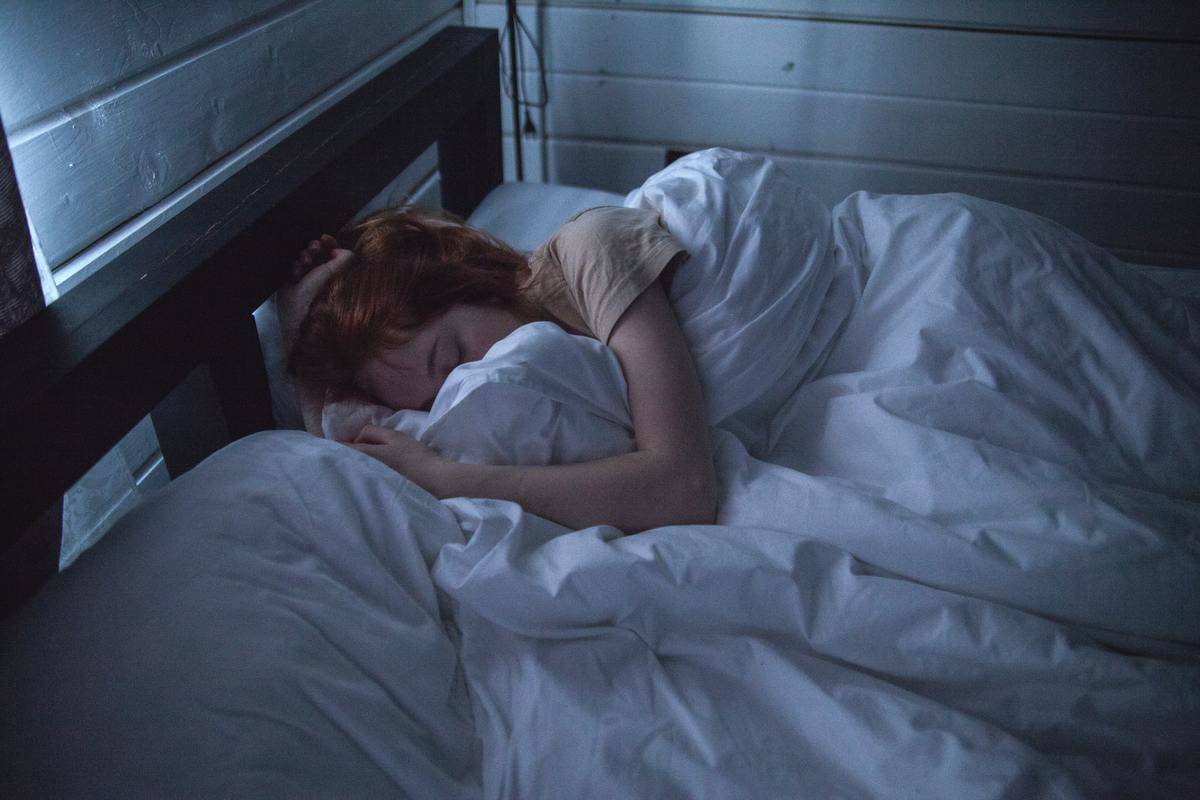 A woman sleeping in bed with low lighting.