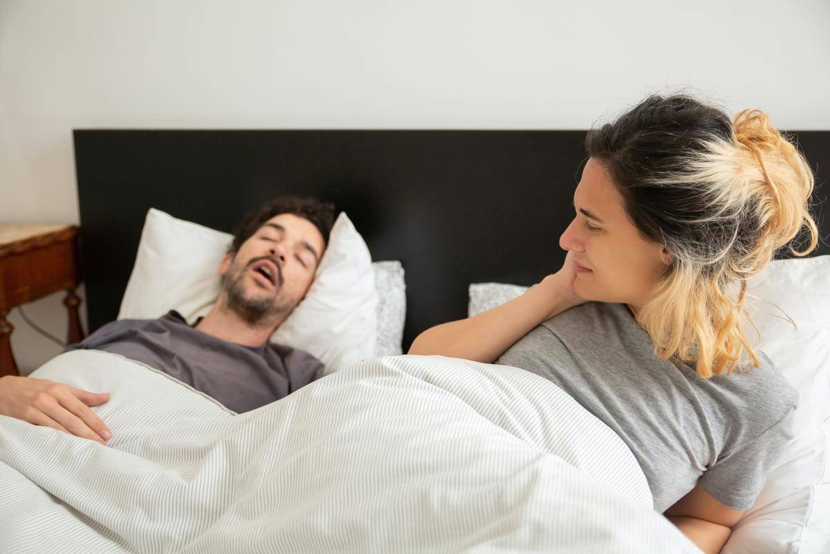 A woman waking up, looking at the man alseep in bed next to her.